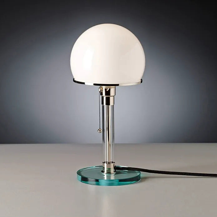 Table lamp with a white glass shade and clear base on a gray surface.